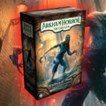 Arkham Horror: The Card Game box art shown prominently in the foreground, with a large illustrated creature and a brick alley scene in the background. Visible brand text includes Arkham Horror and the Card Game.